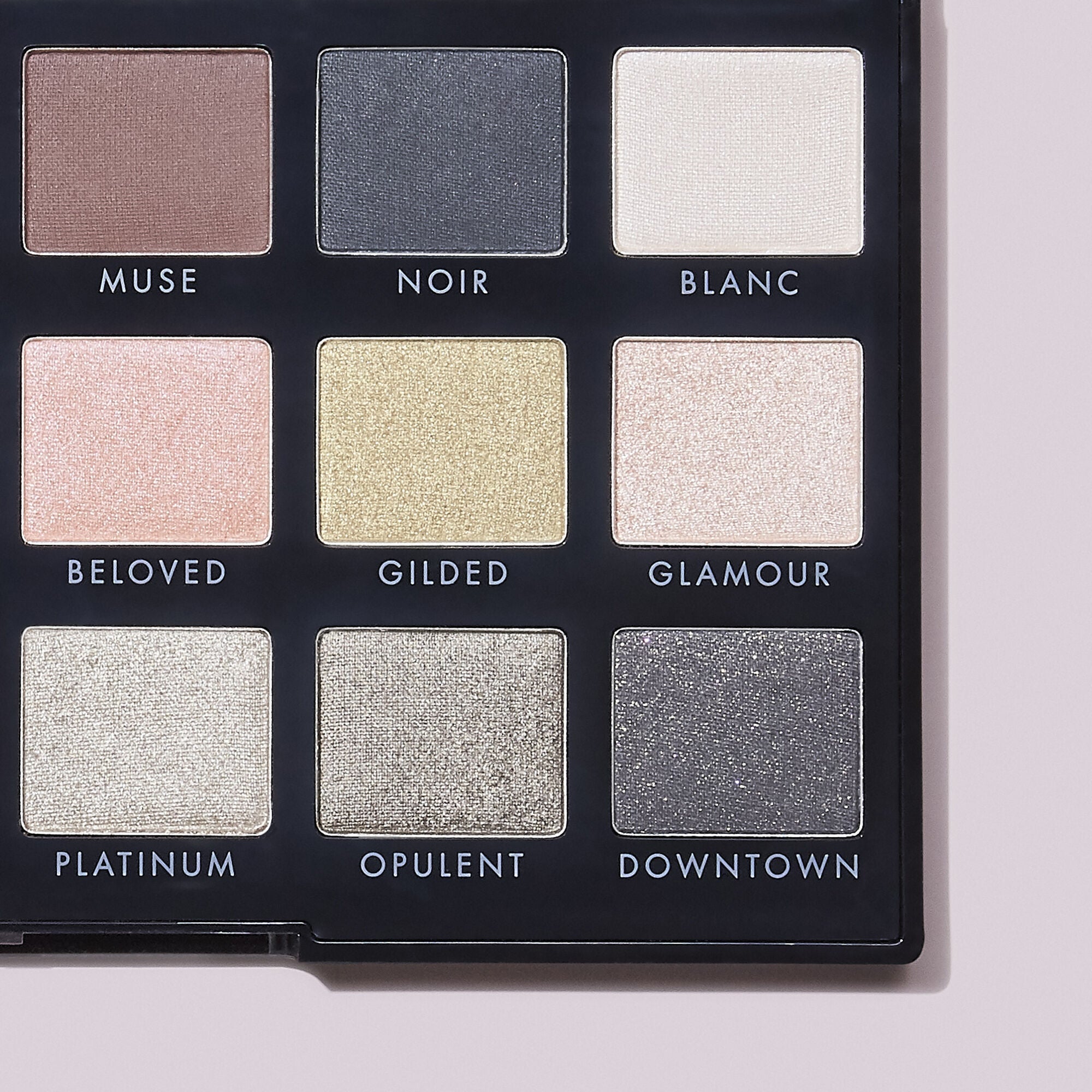 Makeup palette with nine eyeshadow color swatches labeled on a light pink background